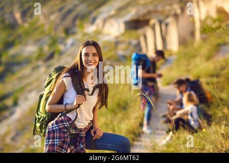 Femme souriante randonneur avec sac à dos regardant l'appareil photo avec un groupe d'amis randonneurs se reposant à l'arrière-plan sur la nature Banque D'Images