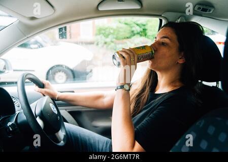 une femme des années 30 boit dans une canette de bière tout en conduisant une voiture Banque D'Images