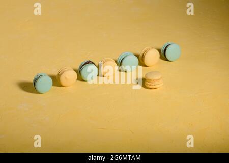 Un groupe de macarons de couleur jaune et bleu-vert sur un fond jaune clair avec lumière dure, espace de copie Banque D'Images