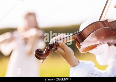 la petite fille joue du violon à l'extérieur avec le jardin en arrière-plan le jour ensoleillé de l'été. Image avec mise au point sélective et espace de copie Banque D'Images