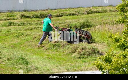 Une promenade à l'essence de taille industrielle derrière la tondeuse pour récolter l'herbe Travailleur isolé vu de l'arrière Santander Cantabria Espagne Banque D'Images