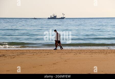 Chalutier revenant au port après une nuit de pêche avec des gens silhouettés marchant le long du rivage Sardinero Santander Cantabria Espagne Banque D'Images