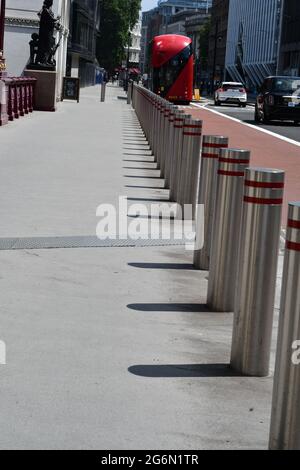 Ligne de bollards argentés et rouges sur une rue animée de Londres le long d'une ligne de bus et des gens au loin le jour de l'été Banque D'Images