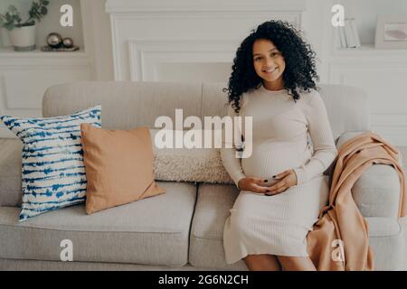 Belle jeune femme enceinte africaine sentant bonheur et amour tout en passant du temps à la maison Banque D'Images