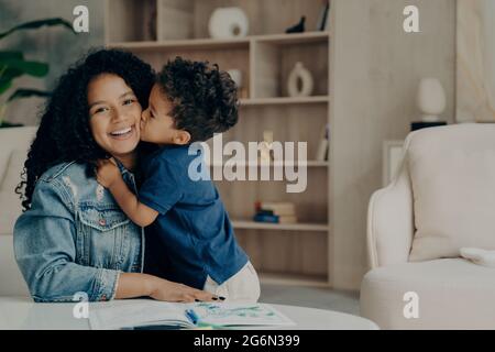 Portrait d'afro-américain mignon garçon dans un polo bleu embrassant la mère et l'embrassant dans la joue Banque D'Images