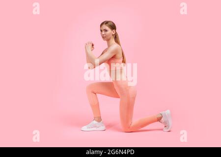 Fitness femme faisant des exercices de fente pour entraîner les muscles de la jambe, femme active faisant un exercice de fente sur une jambe avant, sur fond rose Banque D'Images