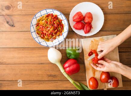 Détail des mains d'une femme qui pelent les tomates avec un couteau. Préparation de poivrons rôtis, un plat typique de cuisine espagnole et andalouse. Banque D'Images