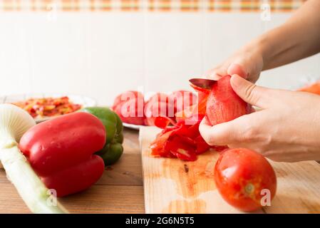 Détail des mains d'une femme qui pelent les tomates avec un couteau. Préparation de poivrons rôtis, un plat typique de cuisine espagnole et andalouse. Banque D'Images