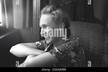 Années 1950, historique, un gros plan, profil d'une jeune fille anglaise attrayante regardant par une fenêtre, Angleterre, Royaume-Uni, portant un haut ou un chemisier, souriant et avec ses cheveux attachés en arrière. Banque D'Images