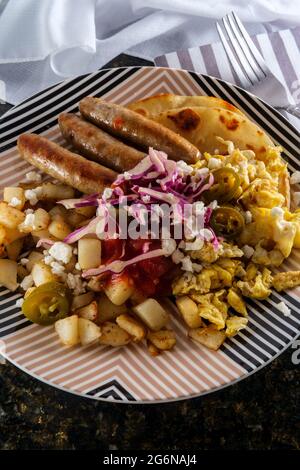 Petit-déjeuner mexicain huevos rancheros oeufs brouillés tostada avec saucisse pommes de terre sauce tomate et queso fresco servi sur tortilla au maïs frit Banque D'Images