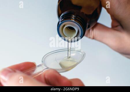 Gros plan des mains des femmes tenant une bouteille de sirop contre la toux expectorant et la versant avec une cuillère de mesure. Concept de soins de santé et de traitement. Flou Banque D'Images