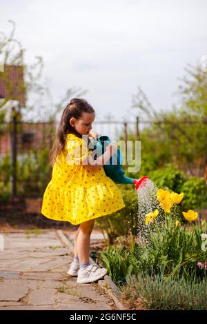 une charmante fille dans une robe jaune qui flirtent dans les eaux du vent tulipes jaunes d'un arrosoir dans le jardin arrière-cour, des éclaboussures d'eau d'un Banque D'Images