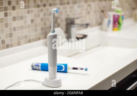 Brosse à dents électrique rechargeable, gros plan. Sur fond de salle de bains en blanc. Robinet d'eau et évier blanc. Banque D'Images