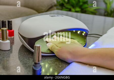 Femme main à l'intérieur de la lampe à ongles sur la table gros plan. Lampe UV pour sécher les ongles selon la méthode du gel. Ongles violets séchés dans une lampe. Banque D'Images