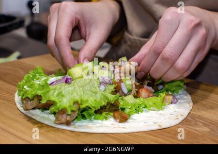 Délicieux petits pains de lave-laves avec poulet frit et légumes sur une planche à découper en bois. Processus de cuisson, gros plan Banque D'Images