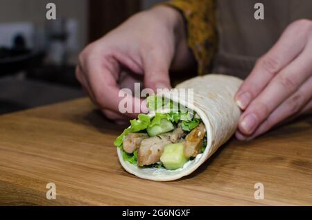 Délicieux petits pains de lave-laves avec poulet frit et légumes sur une planche à découper en bois. Processus de cuisson, gros plan Banque D'Images