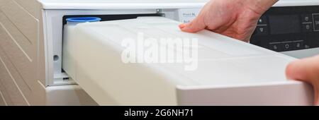 Un récipient pour les condensats du sèche-linge, une femme sort un réservoir avec l'eau accumulée après avoir séché les vêtements du sèche-linge Banque D'Images