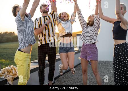 De jeunes amis se délachent sur la terrasse sur le toit au coucher du soleil Banque D'Images