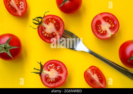 Les tomates rouges et une fourchette se trouvent sur un fond jaune. Belle image. Légumes en tranches et entiers avec couverts, vue du dessus. Banque D'Images