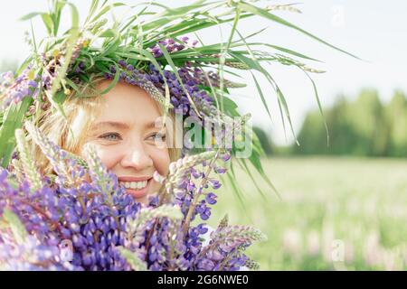 Une fille hippie tenant un bouquet de fleurs sauvages dans ses mains. Une fille cacha son visage derrière un bouquet de lupins. La fille tient un grand bouquet de lupins violets dans un Banque D'Images