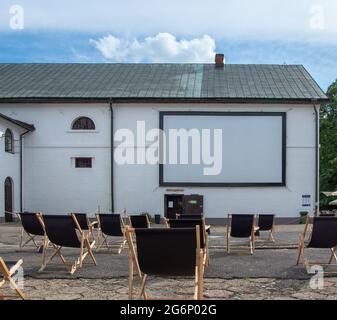 Oper-air, cinéma en plein air dans la cour de la brasserie de Zwierzyniec, Pologne. Rangées de chaises longues simples et noires devant l'écran installé sur le mur. Banque D'Images
