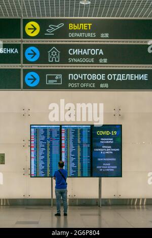 La personne se tient devant l'exposition avec des vols et des informations sur les covides dans le terminal de l'aéroport, sous les panneaux pour la synagogue et le bureau de poste, DME, Moscou, Russ Banque D'Images