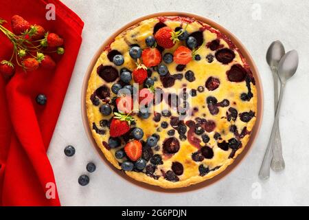 Tarte aux fraises et aux myrtilles décorée de baies fraîches avec une serviette et des cuillères rouges sur fond gris, vue du dessus Banque D'Images
