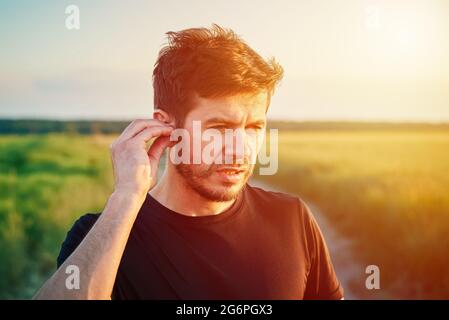 Homme se préparant à courir au coucher du soleil, à allumer les écouteurs sans fil. Portrait de l'homme mlenial actif du caucase Banque D'Images