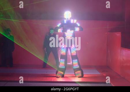 Un danseur dans un costume LED coloré danse avec un laser dans ses mains Banque D'Images