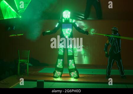 Un danseur en costume LED vert danse avec un laser dans ses mains Banque D'Images