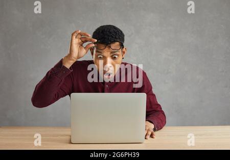 Un homme choqué prend des lunettes de vue regardant avec l'expression du visage stupéfait sur un ordinateur portable Banque D'Images
