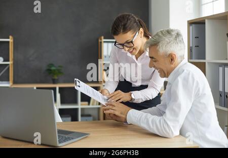 Une femme souriante secrétaire donne des documents papier à son Manager senior ou un contrat à signer. Banque D'Images