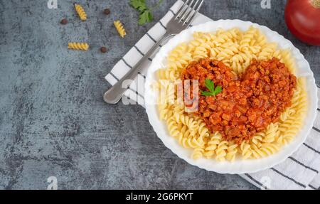 Pâtes fusili avec sauce bolognaise en forme de coeur et persil sur fond sombre Banque D'Images