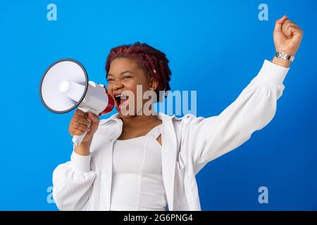 Femme afro-américaine utilisant le mégaphone sur fond bleu Banque D'Images