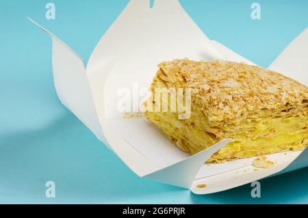 Le gâteau est emballé dans une boîte en papier blanc sur fond bleu clair. Ouvrir l'emballage Kraft avec un morceau de gâteau doux couche. Boîte à lunch écologique. F Banque D'Images