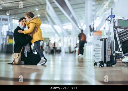 Réunion de la mère et de l'enfant à l'aéroport après une pandémie. Femme dans le masque facial rencontra son fils après son arrivée de voyage à l'aéroport. Banque D'Images