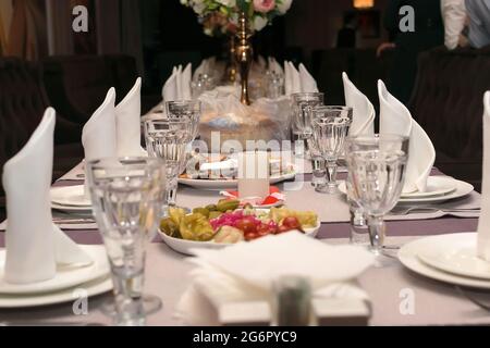 Table dans un restaurant avec une bougie au milieu de la table avec des en-cas, des verres de vin vides, des assiettes propres et des serviettes blanches Banque D'Images