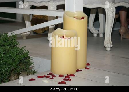 Deux grandes bougies, lampes, se tiennent sur le sol près d'une table de fête et une rose rouge parsemée de pétales Banque D'Images