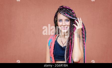 Bonne fille hispanique avec des tresses et tatouage souriant à l'extérieur de l'appareil photo avec un fond coloré Banque D'Images