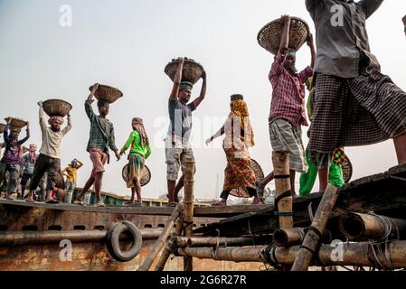 Une chaîne humaine de porteurs transporte du charbon, du sable et du gravier depuis les barges amarrées à la station d'atterrissage d'Aminbazar, sur le fleuve Buriganga, à l'extérieur de Dhaka. Le Bangladesh est diplômé de la catégorie des PMA (pays les moins avancés), grâce en grande partie au travail extrêmement difficile de la main-d'œuvre manuelle bon marché. Un porteur fait entre 80 et 140 USD par mois, selon les sites paylab.com et averagesalarysurvey.com Banque D'Images