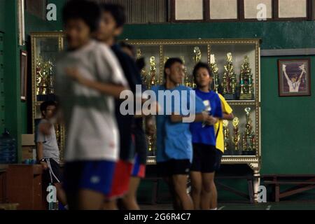 De jeunes joueurs de badminton se réchauffent lors d'une séance d'entraînement au club de badminton Jaya Raya à Jakarta, en Indonésie, photographiés dans un fond d'armoire à trophées et une photo de l'ancien joueur vedette du club, Susi Susanti, médaillé d'or olympique. Banque D'Images