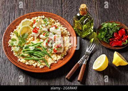 Bacalhau com todos, morue au bulgur, haricots verts cuits à la vapeur, saupoudrée de piments forts et d'oignons de printemps sur une assiette rustique, sur une table en bois, por Banque D'Images