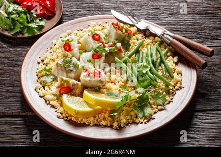 Bacalhau com todos, morue au bulgur, haricots verts cuits à la vapeur, saupoudrée de piments forts et d'oignons de printemps sur une assiette rustique, sur une table en bois, por Banque D'Images