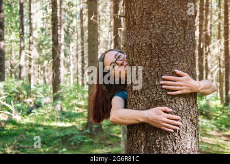 Une jeune femme gaie embrasse un arbre dans un parc ou une forêt. Banque D'Images