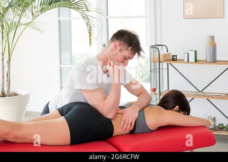 Ostéopathe faisant un massage myofascial carré des reins en utilisant son coude pour appliquer une pression sur la colonne vertébrale et le bas du dos d'une femme yong dans sa clinique Banque D'Images