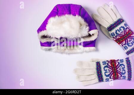 Chapeau violet chaud à platte d'hiver avec rabats et gants tricotés en laine colorés sur fond violet blanc. Vue de dessus, maquette pour marque, copie s. Banque D'Images