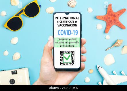 Concept de certificat de vaccination contre le coronavirus ou de passeport vaccinal pour les voyageurs. COVID-19 immunité e-passeport dans l'application mobile pour smartphone pour les voyages internationaux. Fond bleu avec lunettes de soleil, coquillages et avion. Photo de haute qualité Banque D'Images