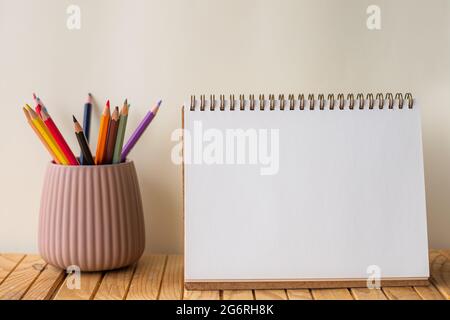 Vider le carnet spirale ouvert à côté de la pile colorée de crayons dans le conteneur sur le bureau. Journal ouvert vierge avec des stylos de différentes couleurs à l'intérieur du support Banque D'Images