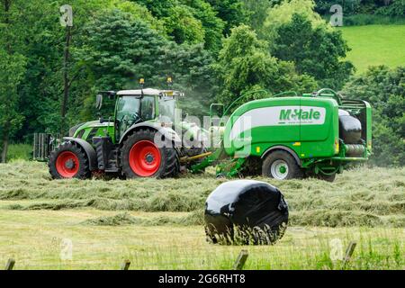 Production de foin et d'ensilage (agriculteur travaillant dans un tracteur agricole dans un champ rural pittoresque, recueillant de l'herbe sèche, balle ronde enveloppée dans une presse à balles) - Yorkshire England, Royaume-Uni. Banque D'Images