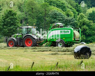 Production de foin et d'ensilage (agriculteur travaillant dans un tracteur agricole dans un champ rural, ramassage de l'herbe sèche coupée, balle ronde non enveloppée dans une presse à balles) - Yorkshire England, Royaume-Uni. Banque D'Images